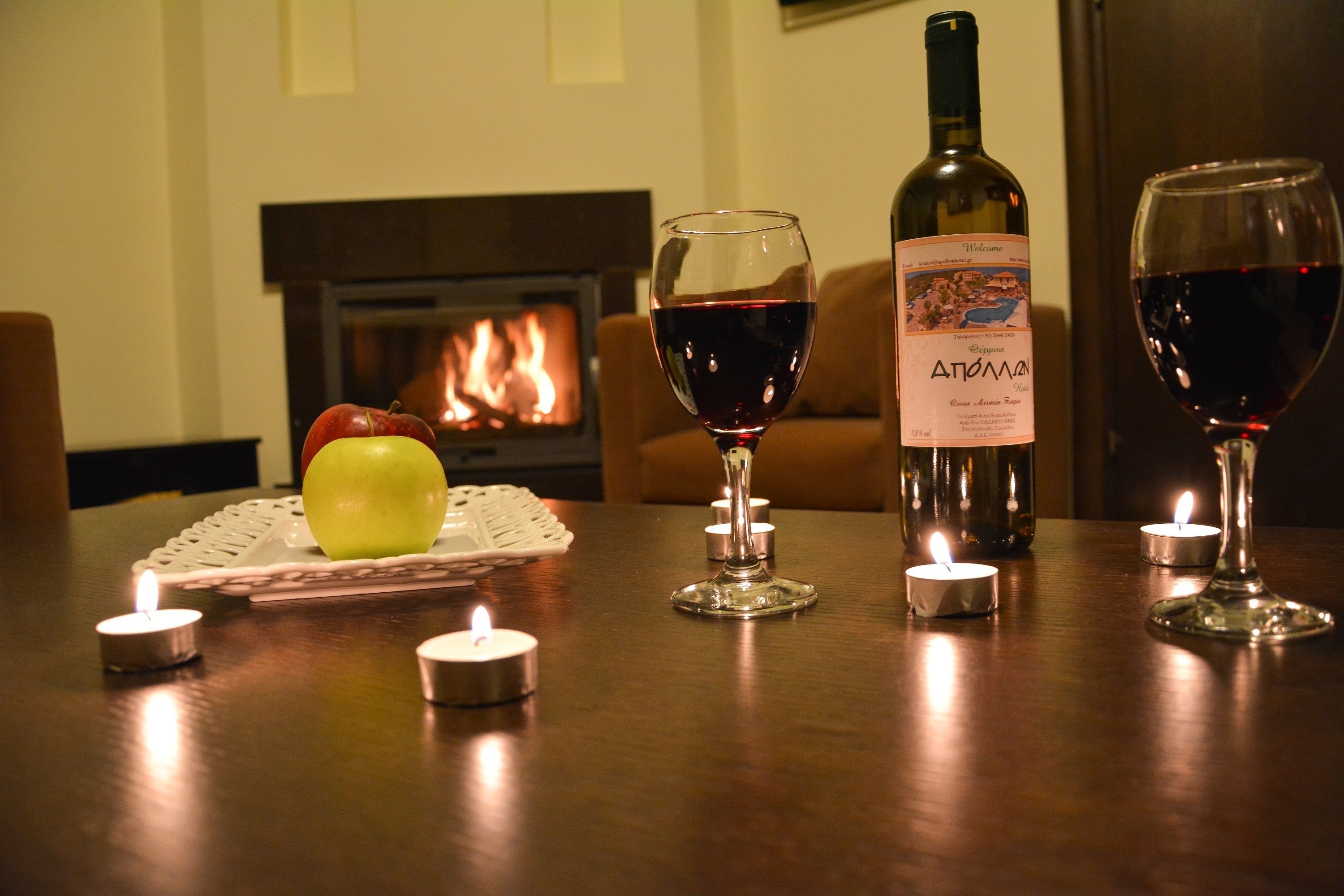 Una mesa con una botella de vino, dos copas de vino, una vela encendida y una manzana sobre un posavasos.