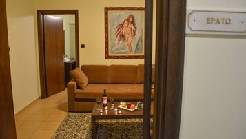 A living room with a brown sofa, a coffee table with a bottle and glasses, and a painting on the wall.