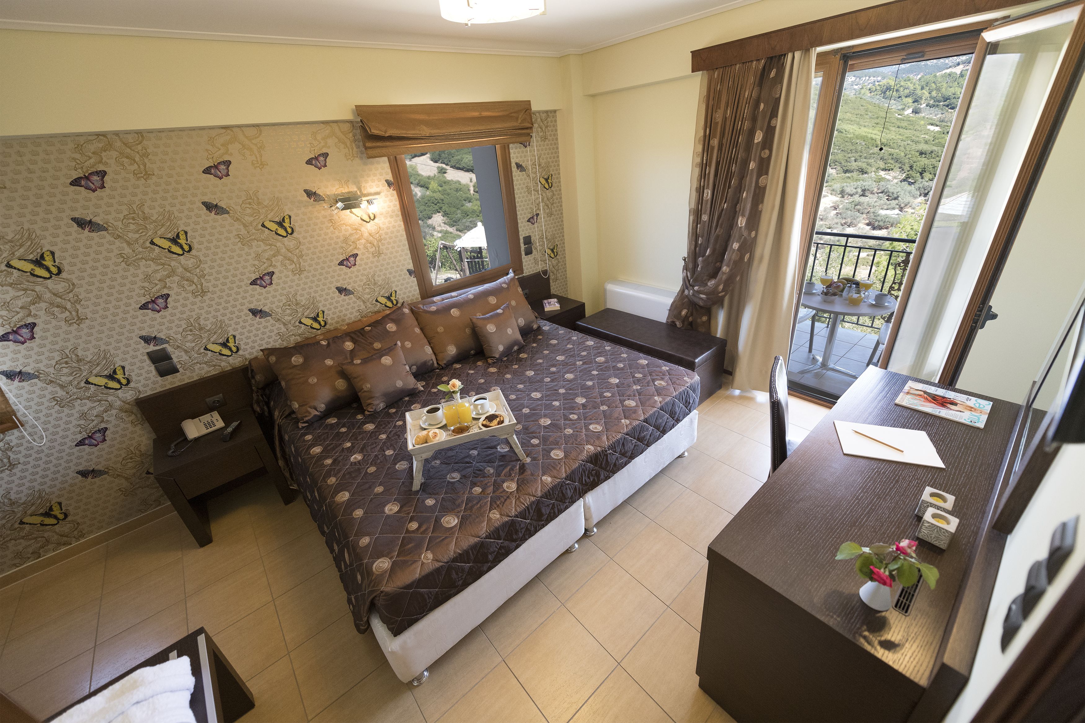 Een slaapkamer met een bed, nachtkastjes, een klein bureau en een balkon met een tafel en stoelen.