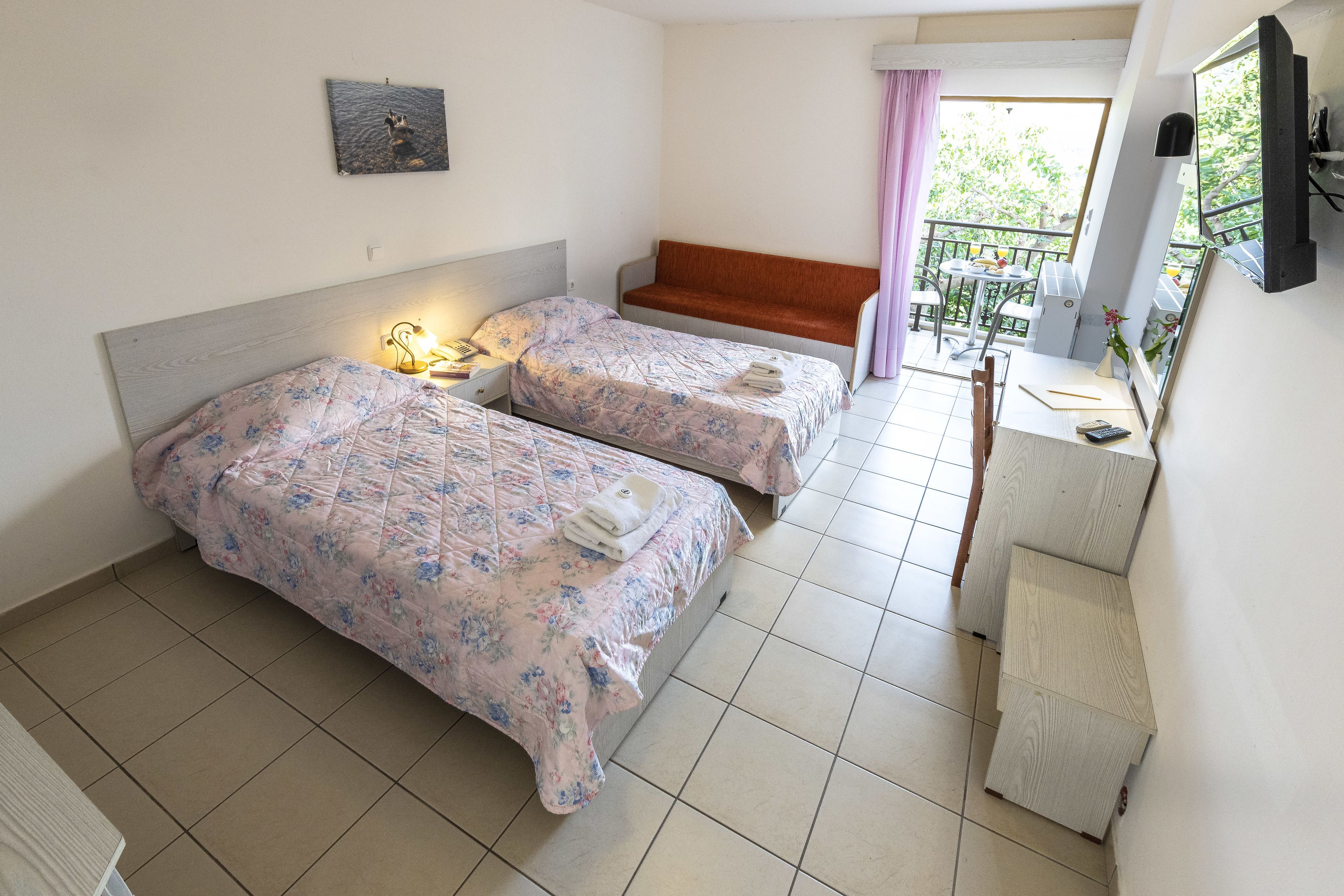 Una camera da letto con due letti, una panca, una scrivania e un balcone con vista.