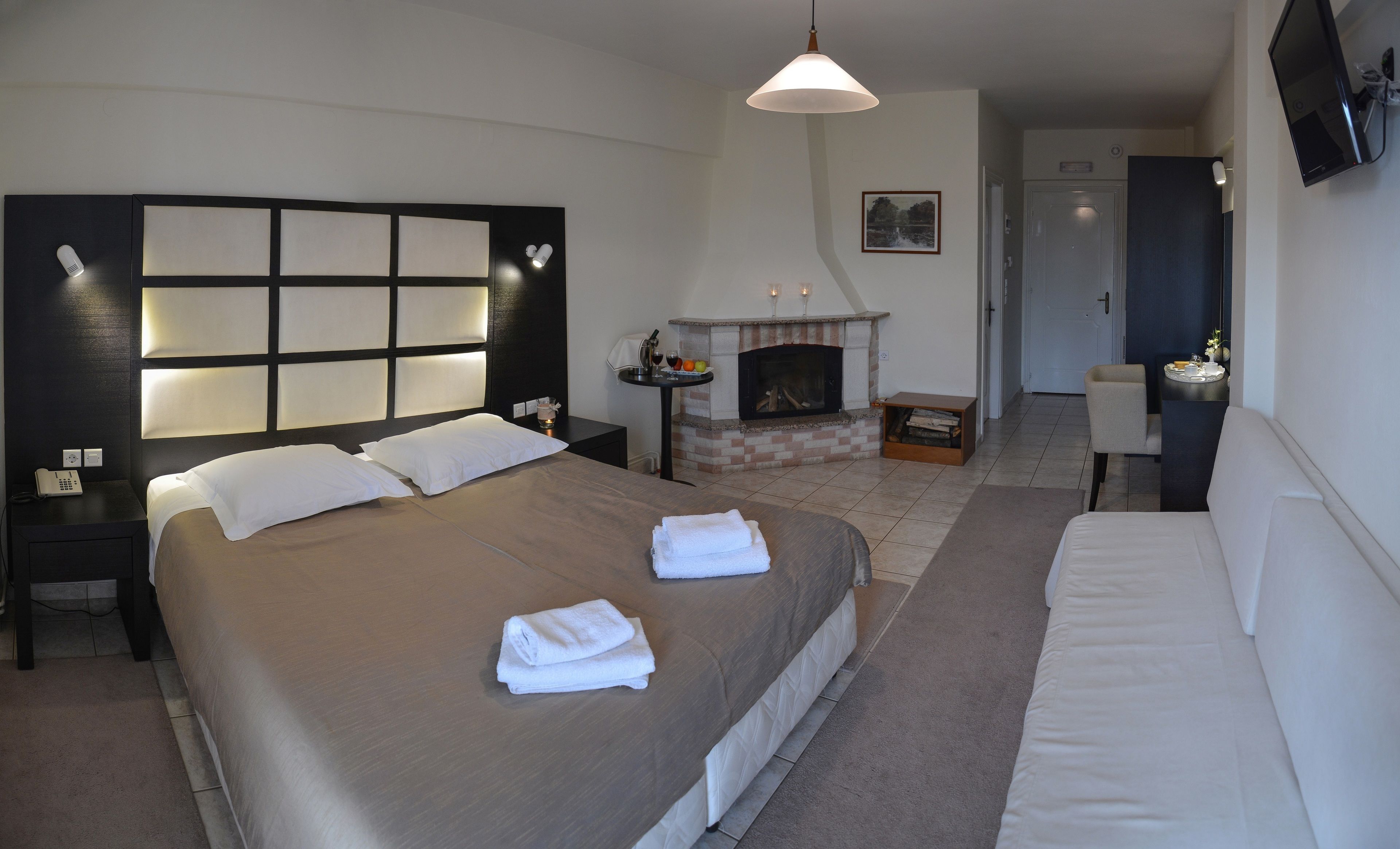 A hotel room with a large bed, bedside tables, a fireplace, and a TV mounted on the wall.