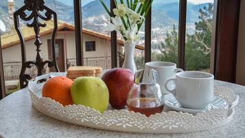 A tray with fruits, a vase with flowers, and cups on a table with a view of mountains.
