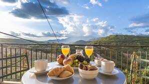 Une table avec des aliments pour le petit-déjeuner et deux verres de jus d’orange, sur un balcon offrant une vue sur la montagne.