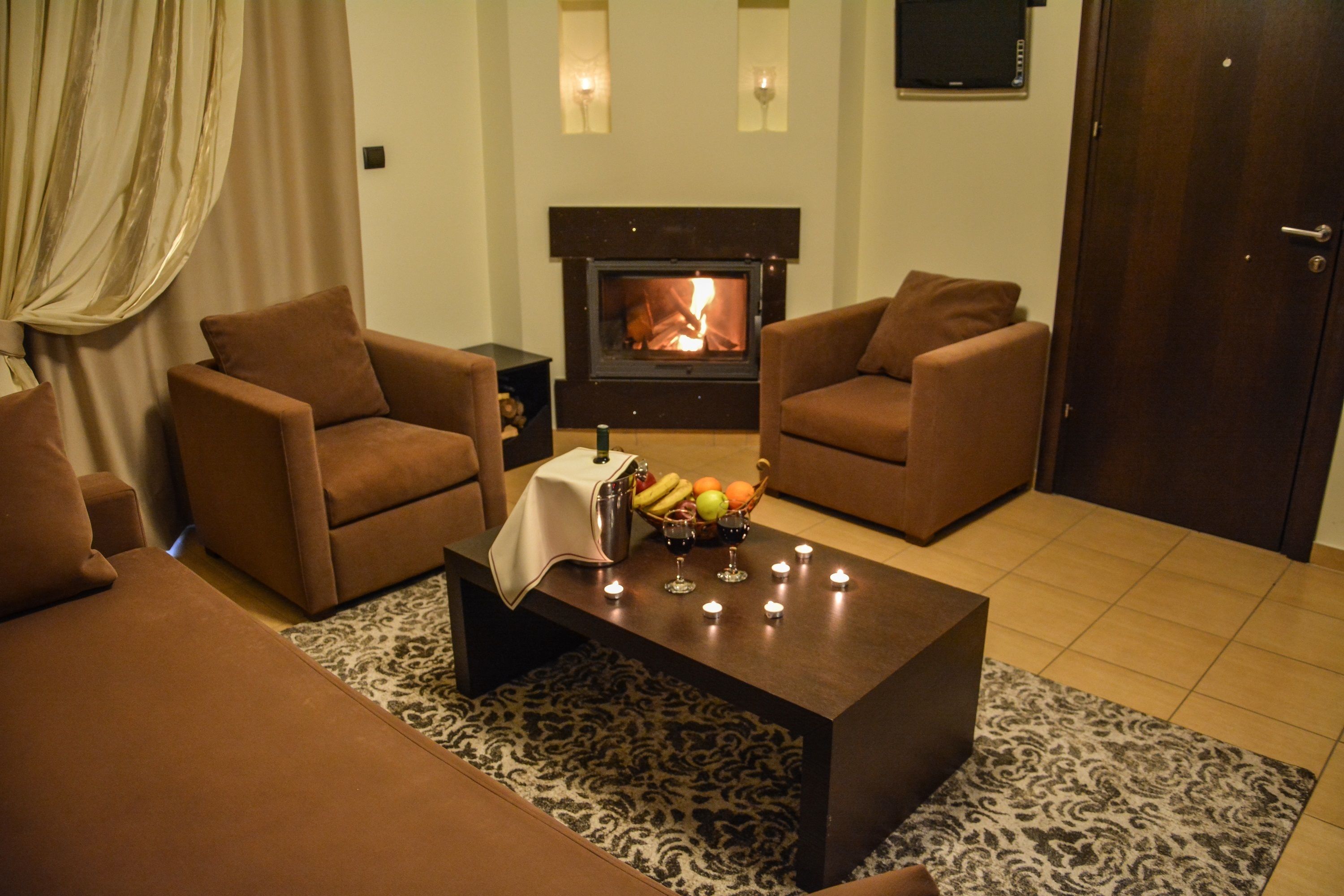 A living room with two brown sofas, a coffee table with fruit and wine glasses, a fireplace, and a patterned rug.