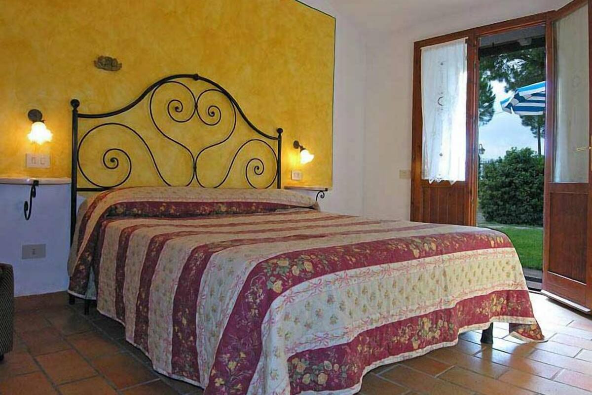 A bedroom with a bed, a yellow wall, a window with curtains, and a view of greenery outside.