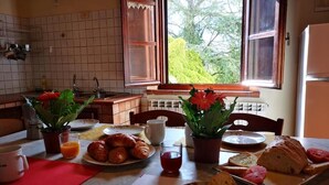 Una mesa de desayuno con cruasanes, pan, tomates y un periódico.