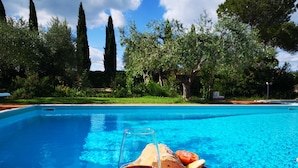 Vista de la piscina con una mesa dispuesta para una comida, incluyendo pan, tomates y una copa de vino tinto.