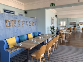Un restaurante con pared azul, mesas de madera y asientos acolchados en azul y amarillo.
