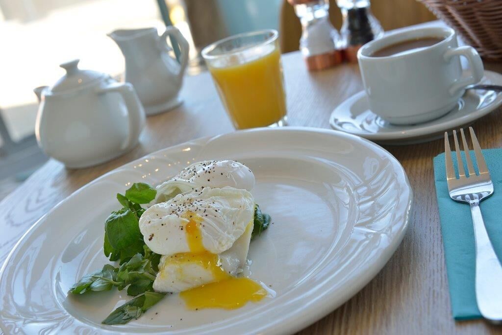 A breakfast setting with a poached egg on a plate, a cup of coffee, and a pitcher of orange juice.