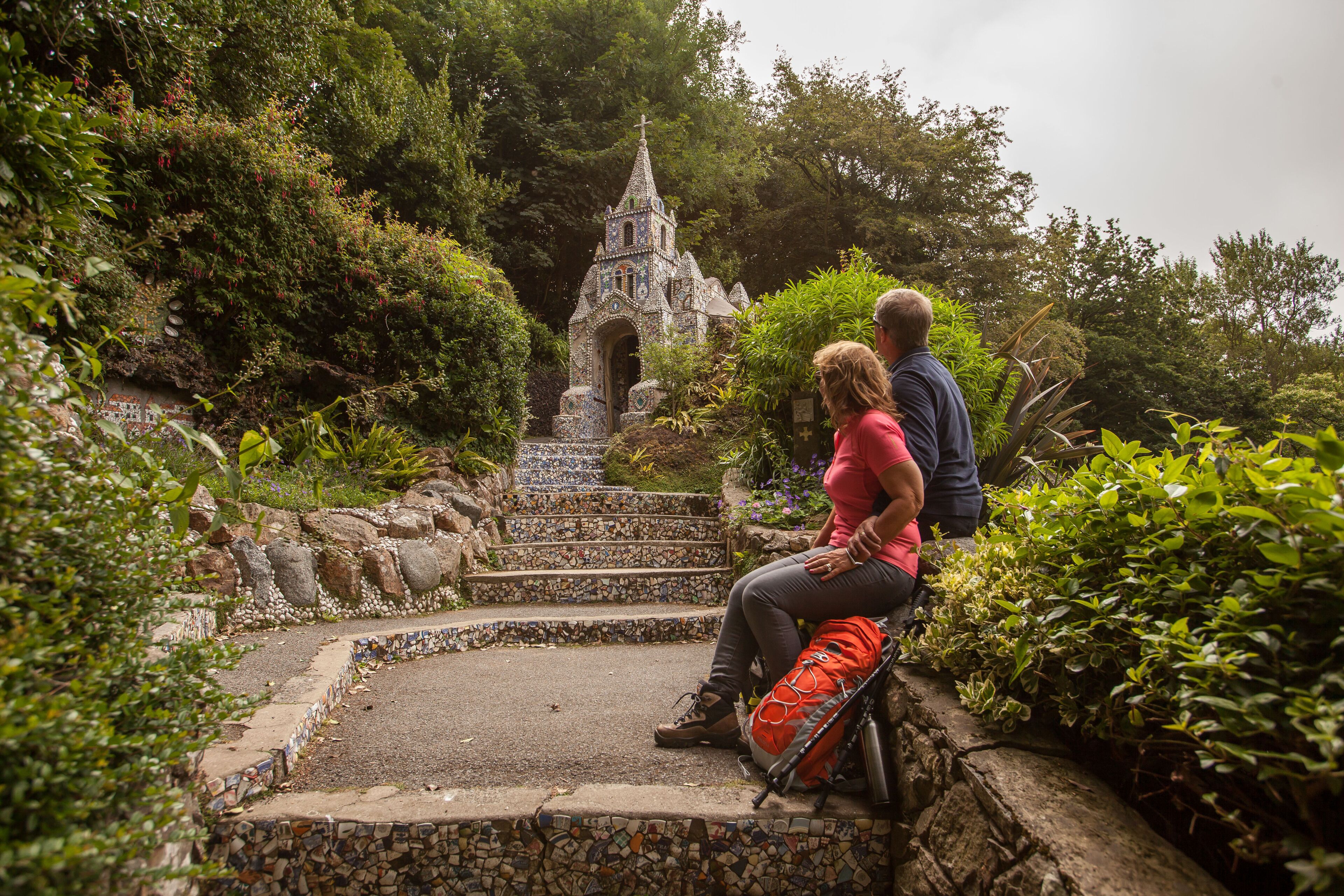 A couple sitting on a stone bench in a garden with a decorative building in the background.