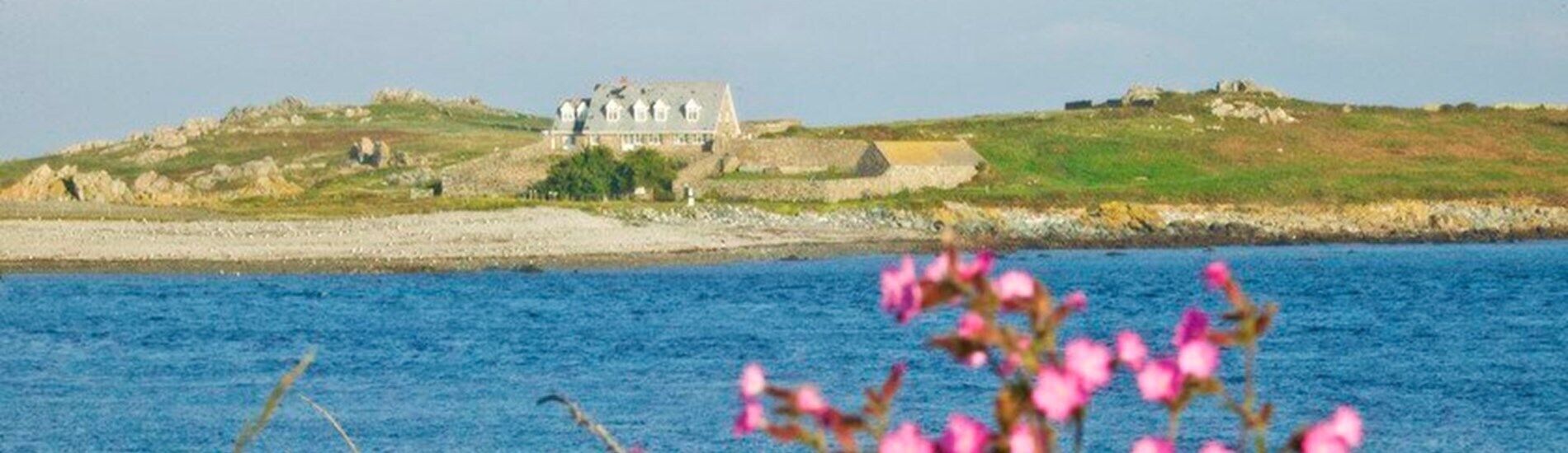 Una casa costera con vista al mar y una colina cubierta de hierba al fondo.