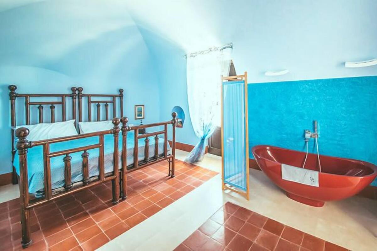A bedroom with a wooden bed, a red bathtub, and a small table with toiletries.