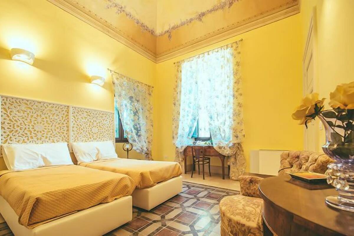 A hotel room with two beds, a desk, a chair, and a vase with flowers.