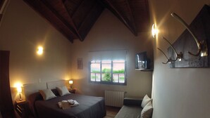 Un dormitorio con cama, mesitas de noche, ventana, radiador y televisor montado en la pared.