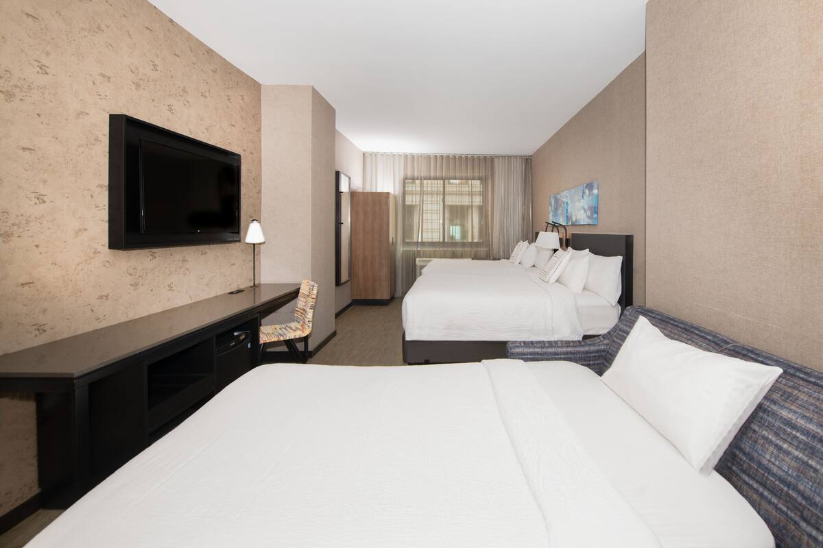 Une chambre d’hôtel avec un grand lit, un bureau avec une chaise, une télévision et une fenêtre avec des rideaux.