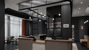 A modern hotel reception area with a curved desk, seating, and a large window with curtains.