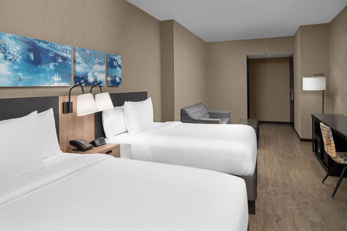 Ein Hotelzimmer mit zwei Betten, einem Schreibtisch, einem Stuhl und einem Telefon auf dem Nachttisch.