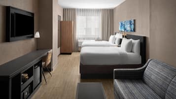 Habitación de hotel con televisión, dos camas, sofá, escritorio y ventana con cortinas.
