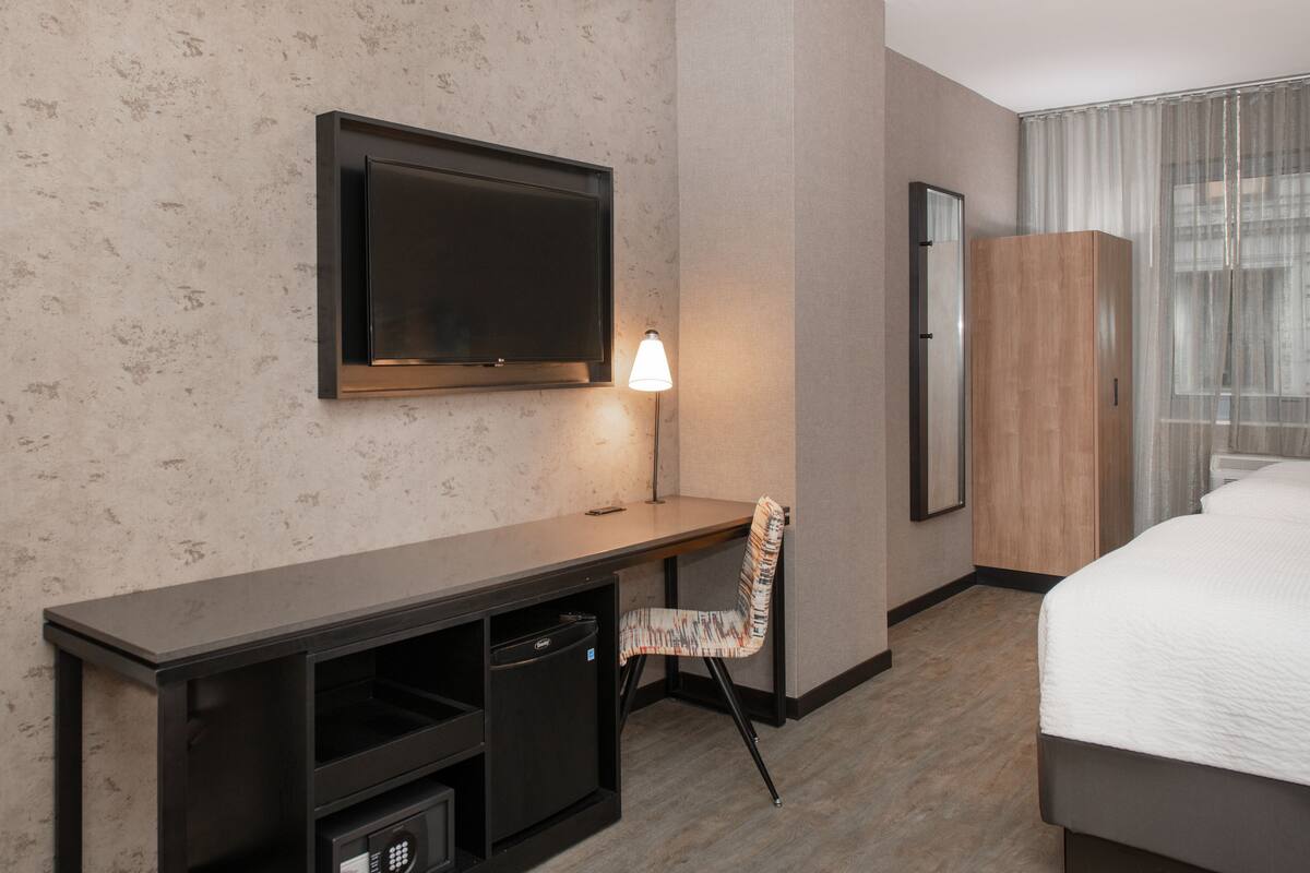 Une chambre d’hôtel équipée d’un téléviseur à écran plat fixé au mur, d’un bureau avec une chaise, d’une armoire et d’un lit.