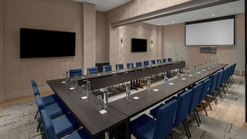 Una sala de conferencias con una larga mesa, sillas azules y una pantalla para proyector.