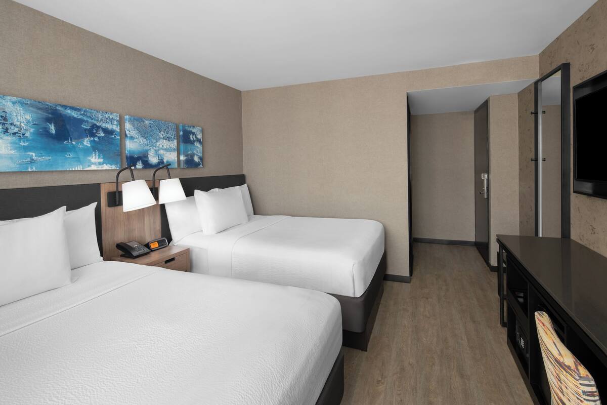 Une chambre d’hôtel avec deux lits, un bureau avec une lampe, une télévision et des œuvres d’art accrochées au mur.