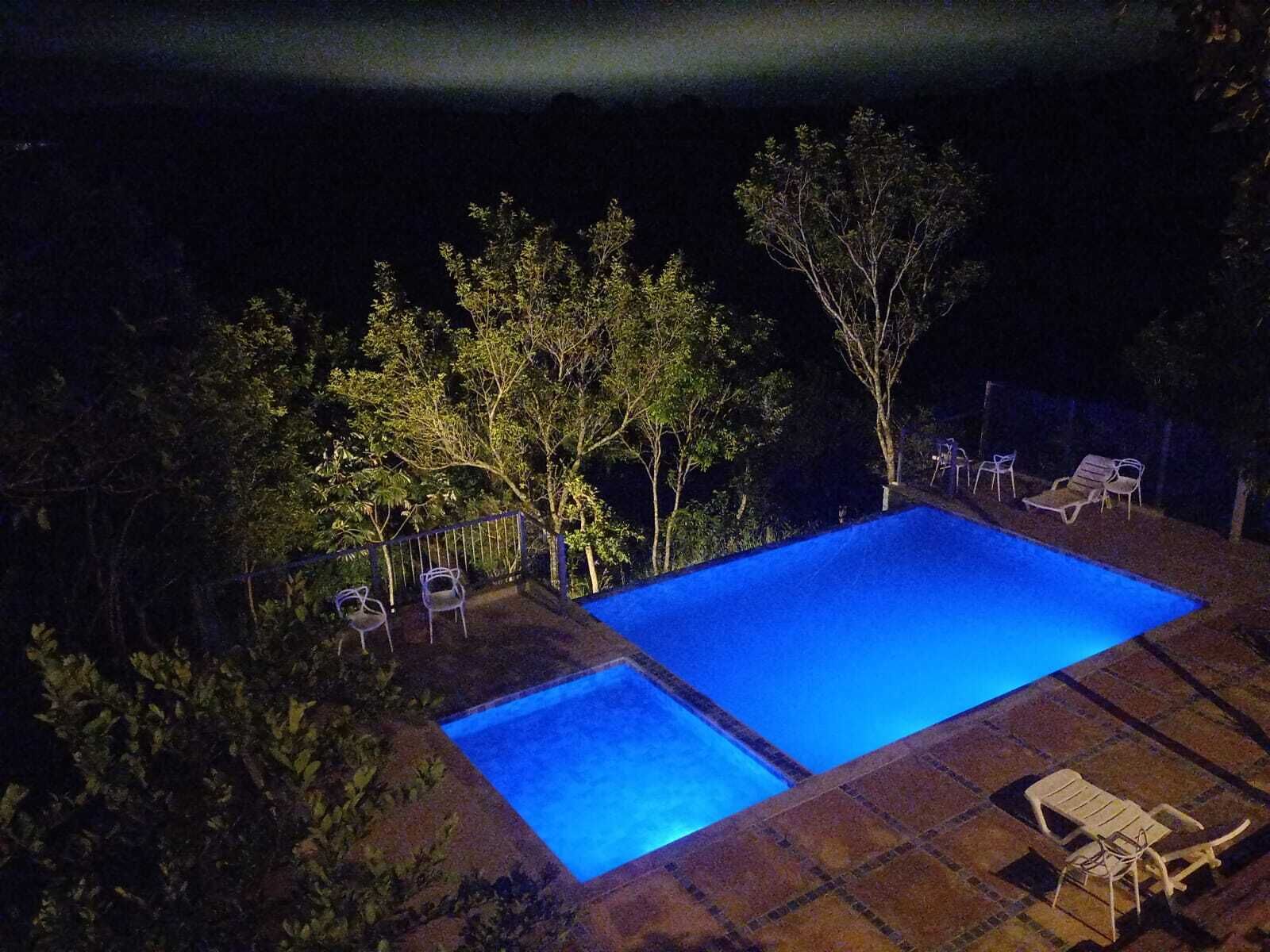 Piscina rectangular con dos áreas separadas, rodeada de árboles y una valla.