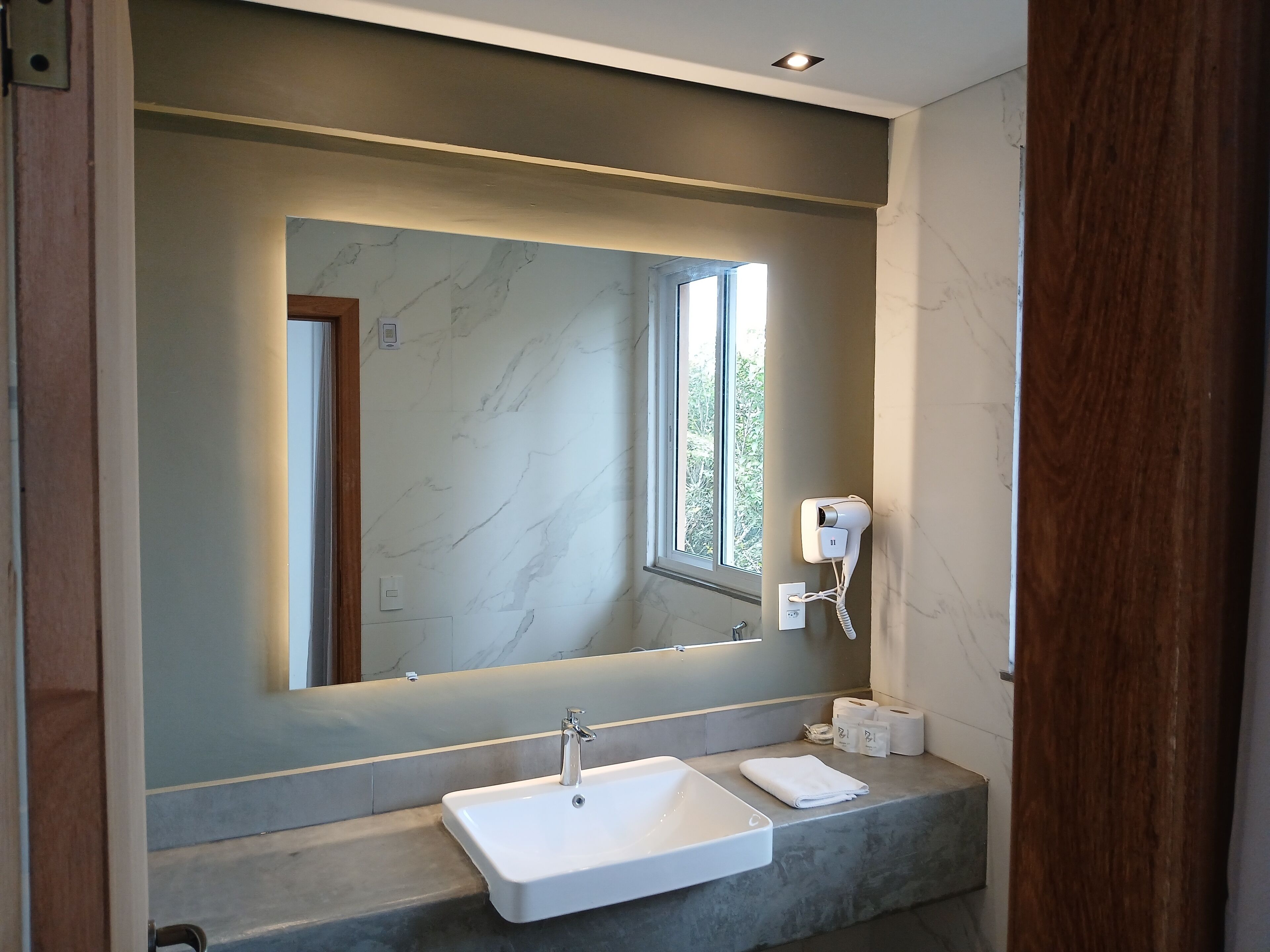 A modern bathroom with a large mirror, a built-in sink, and a hairdryer mounted on the wall.
