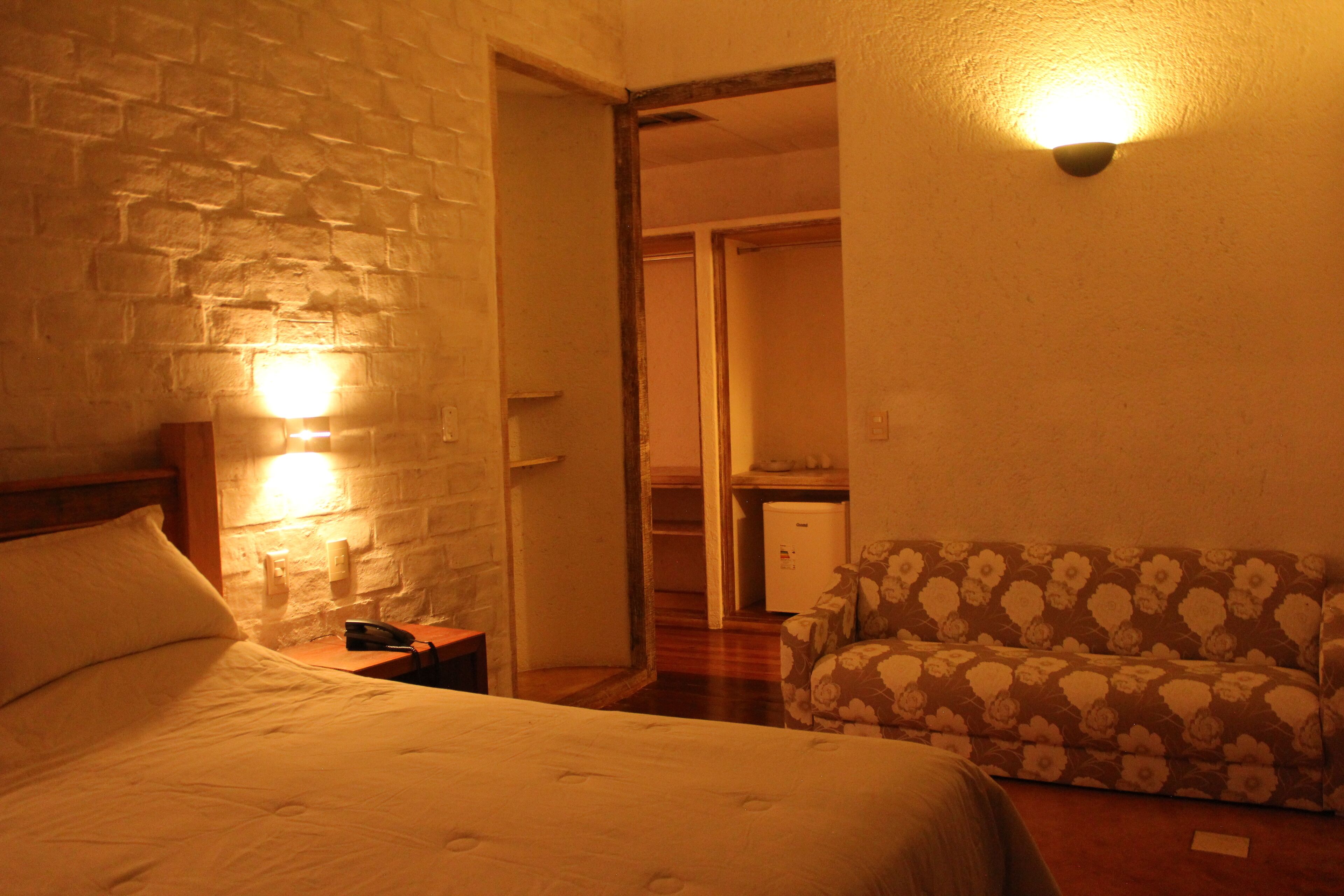 Habitación de hotel con cama, mesita de noche, teléfono, sofá y lámpara de pared.