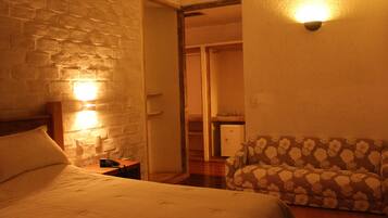 Habitación de hotel con cama, mesita de noche, teléfono, sofá y lámpara de pared.