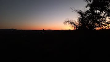 Un atardecer sobre un paisaje llano, con siluetas de árboles y luces a lo lejos.