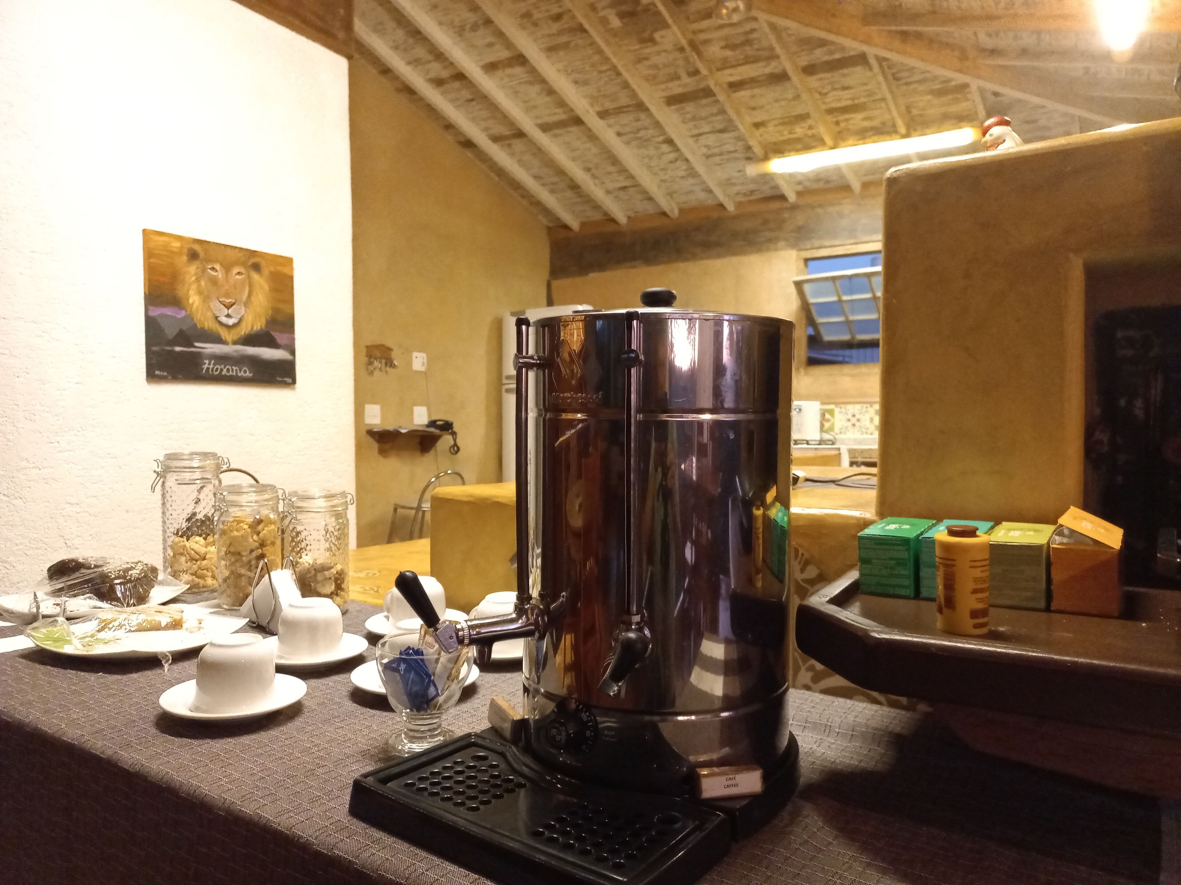A coffee station with a coffee maker, jars of snacks, and a lion painting on the wall.