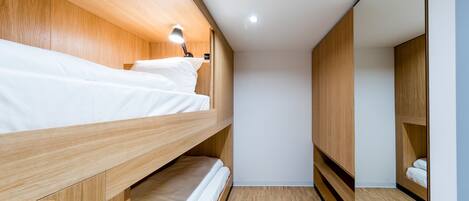 A bunk bed room with wooden walls, a ceiling light, and a small bedside table.