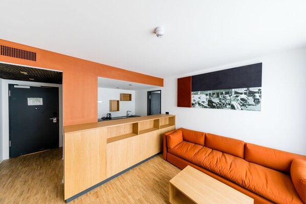 A modern reception area with a wooden desk, a black door, and an orange sofa. - mk | hotel rüsselsheim (Ruesselsheim)