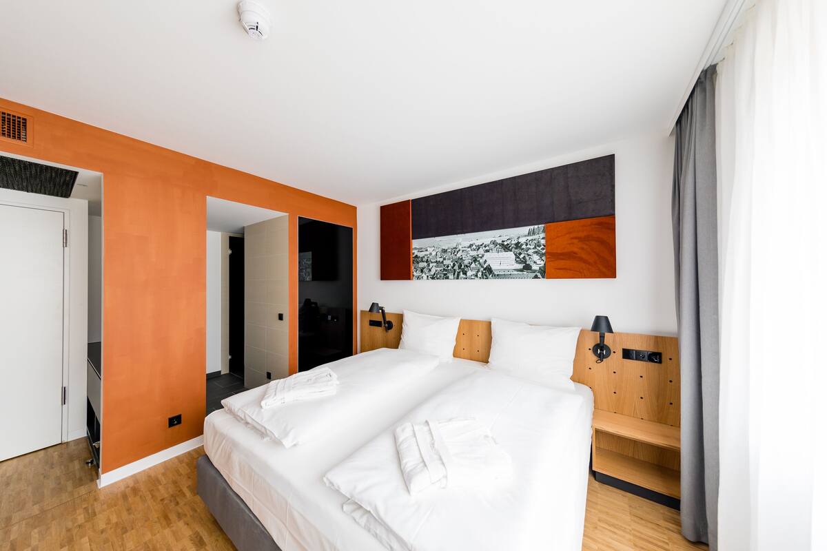 Una habitación de hotel moderna con una cama grande, un cabecero de madera y una obra de arte colgada en la pared.