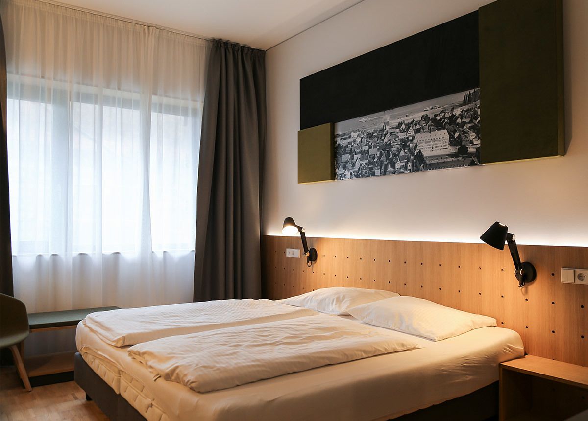 Hotellihuone, jossa on suuri sänky, kaksi yöpöytälamppua, työpöytä ja ikkuna, jossa on verhot.