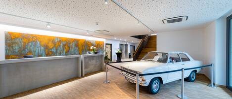 A reception area with a vintage car on display, a large abstract painting, and a staircase leading to an upper level.