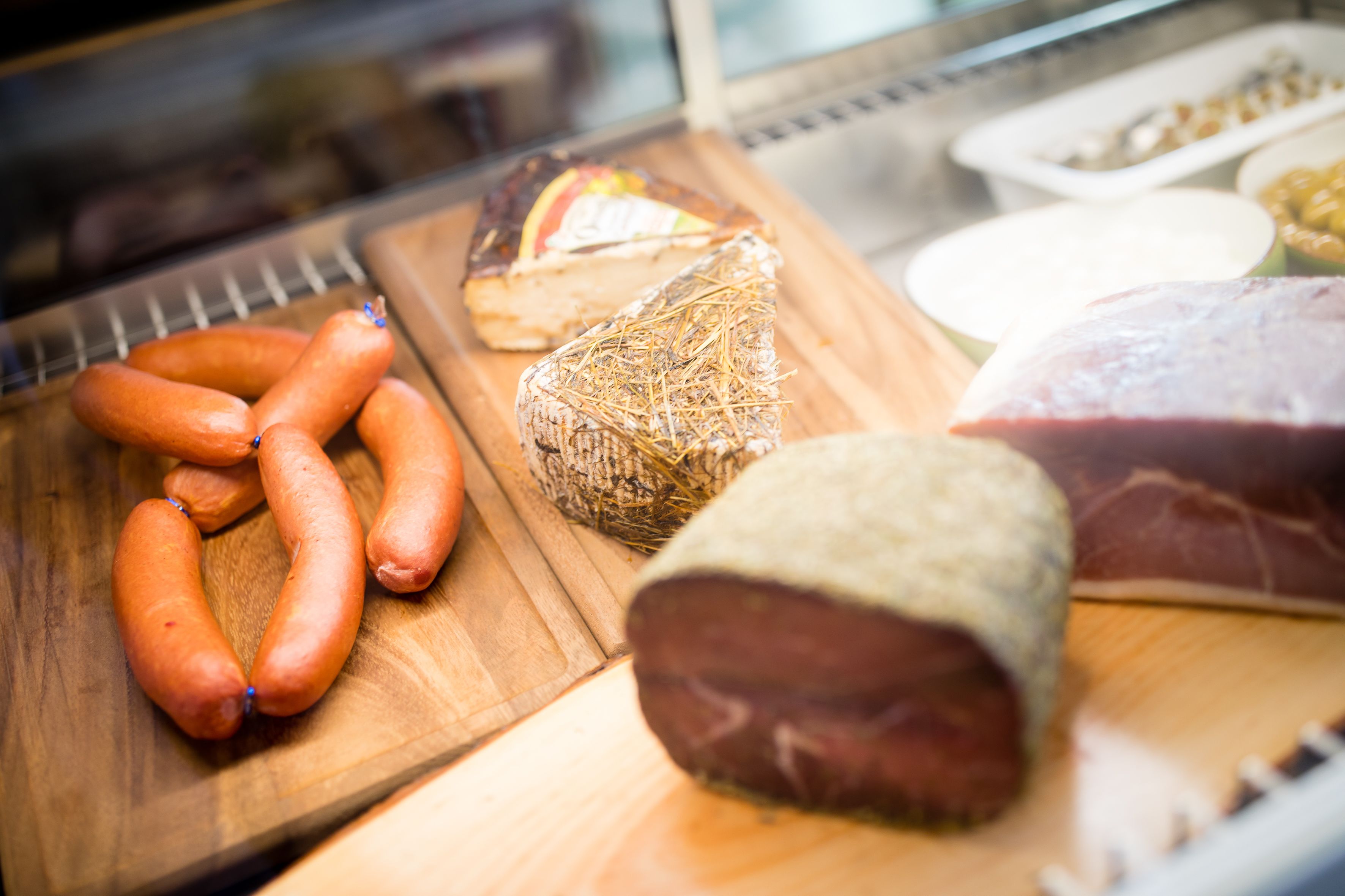 A variety of meats on a wooden cutting board, including sausages, a wrapped meat, and a large piece of meat.