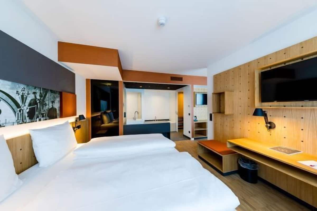 Una habitación de hotel con una cama grande, un escritorio, un televisor y una kitchenette.
