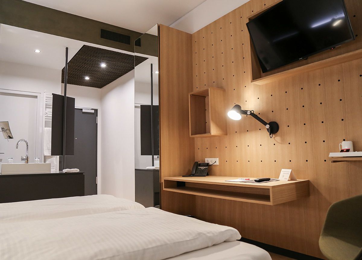 Une chambre d’hôtel moderne équipée d’un lit, d’un bureau avec une lampe, d’un téléviseur fixé au mur et d’un décor mural en panneaux de bois.