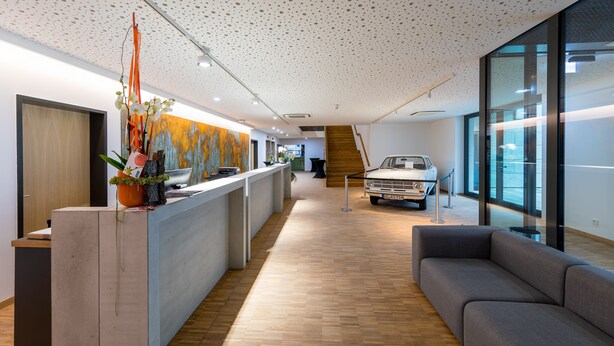 Un espace d’accueil moderne avec un plancher en bois, un comptoir d’accueil, un canapé gris et une voiture ancienne.