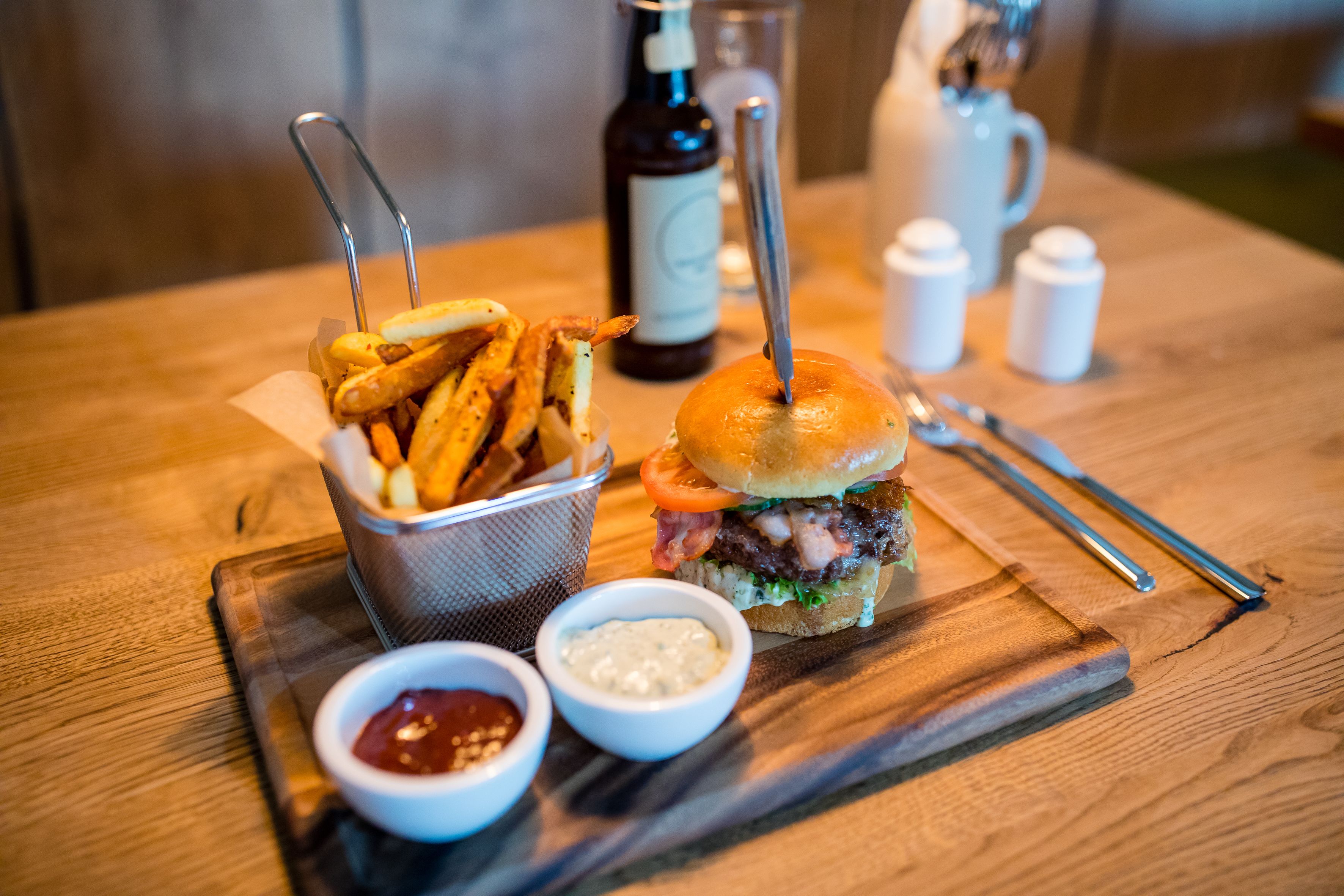 Una comida con una hamburguesa, papas fritas y dos salsas para mojar, sobre una mesa de madera.