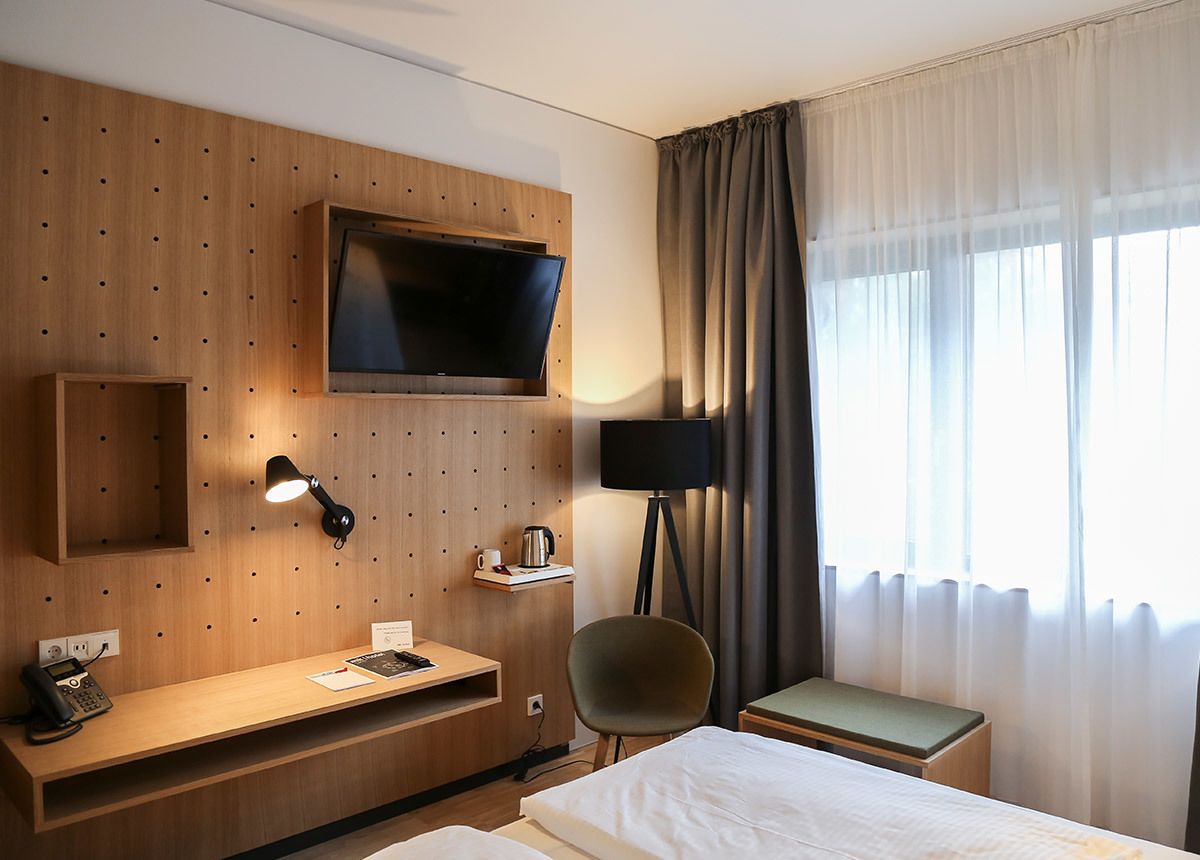 Hotelkamer met een bed, een bureau met telefoon, een aan de muur bevestigde televisie, een stoel en een klein tafeltje.