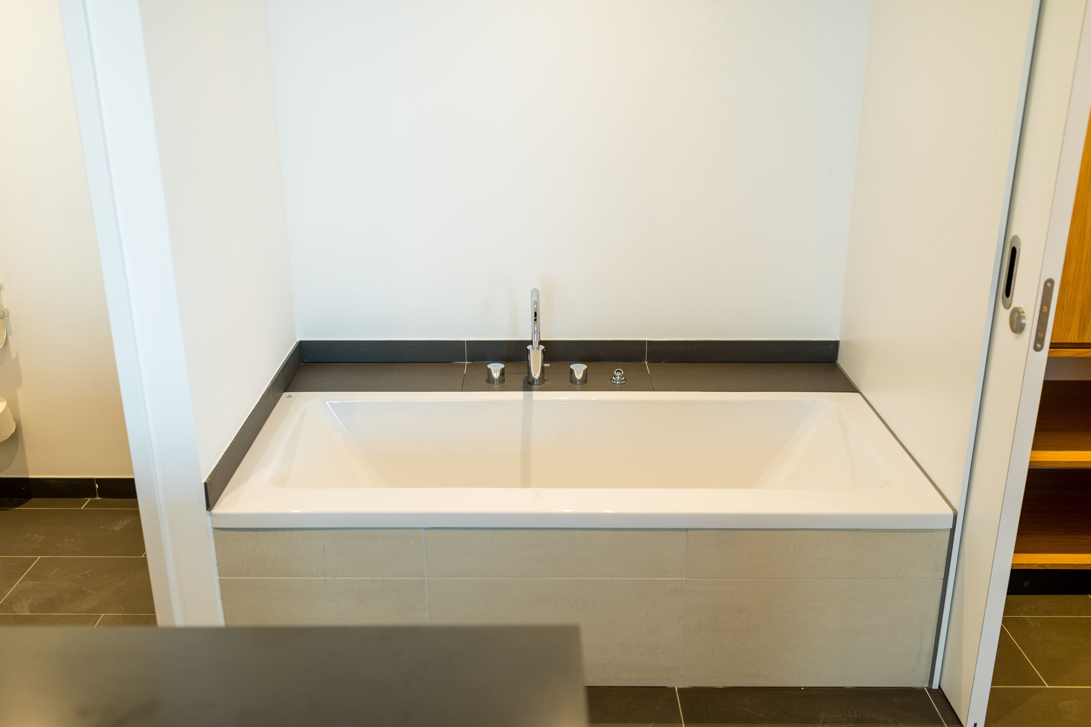 Un baño moderno con una bañera blanca, una encimera negra y suelo de baldosas.
