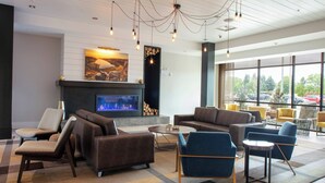 A modern lounge area with sofas, chairs, a fireplace, and large windows offering a view of the outdoors. - SpringHill Suites by Marriott Great Falls (Great Falls)