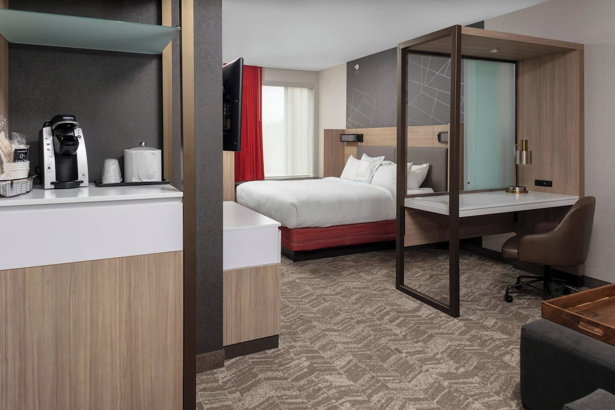 A modern hotel room with a bed, a desk, a coffee maker, and a TV.