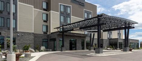 A modern hotel entrance with a covered walkway, stone facade, and a clear sky.