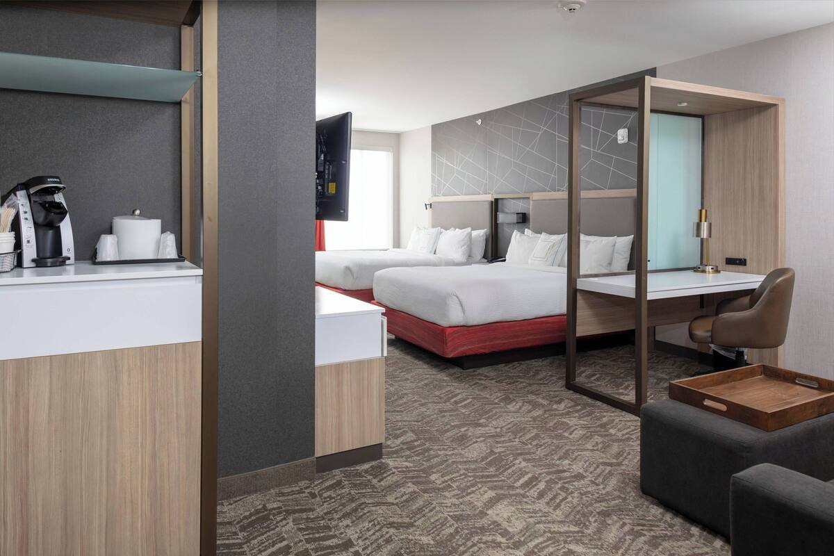 A modern hotel room with a bed, a desk, a chair, and a coffee machine.