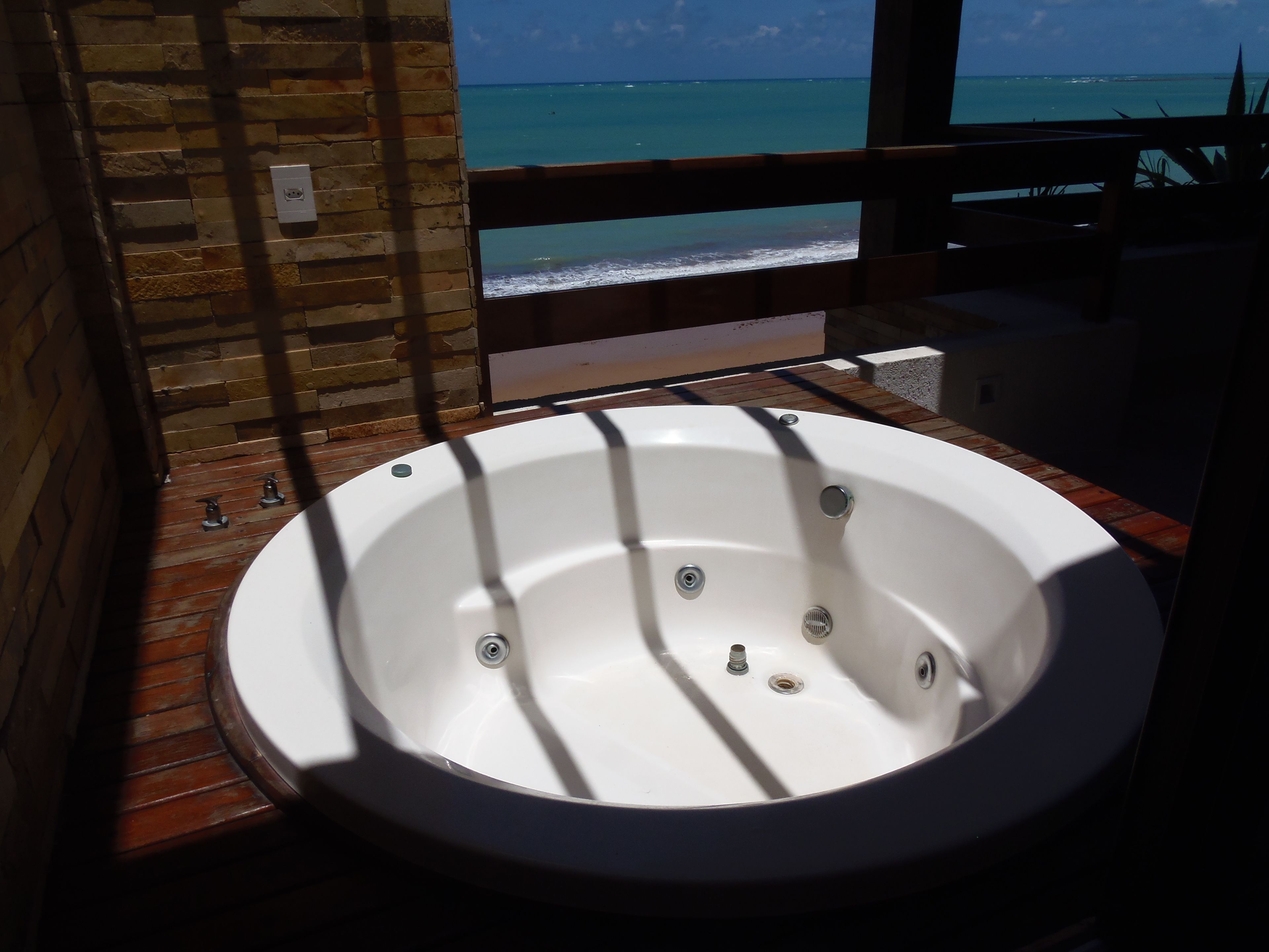 A bathroom with a large bathtub, wooden flooring, and a view of the ocean through a window.