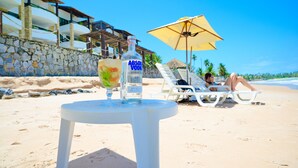 A beachside setting with a table, a bottle of Absolut Vodka, and a person relaxing under a beach umbrella. - Waterfront Apart Hotel (Maceió)
