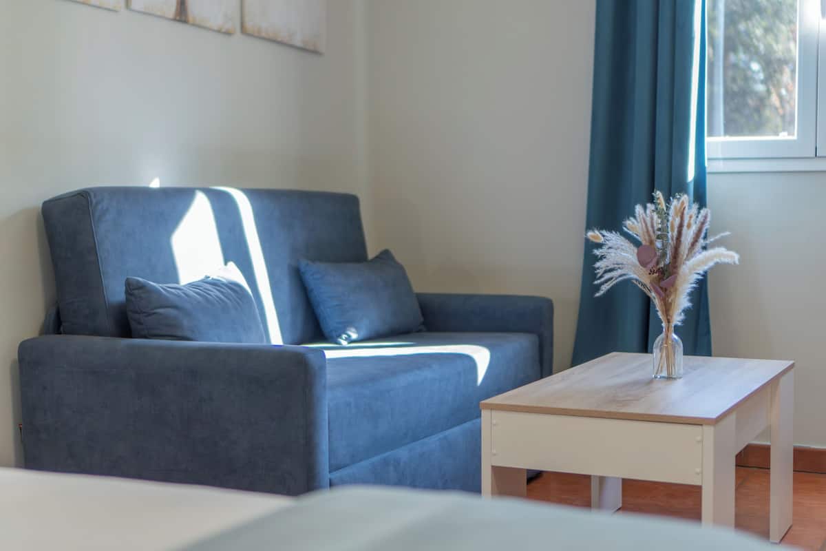 Ein modernes Wohnzimmer mit einem grauen Sofa, einem kleinen Holztisch und einer Vase mit getrockneten Blumen.